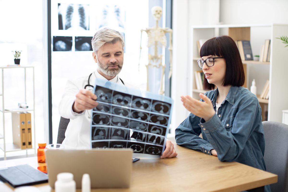 Doctor holding a sheet of MRI scans while talking with a patient at his desk